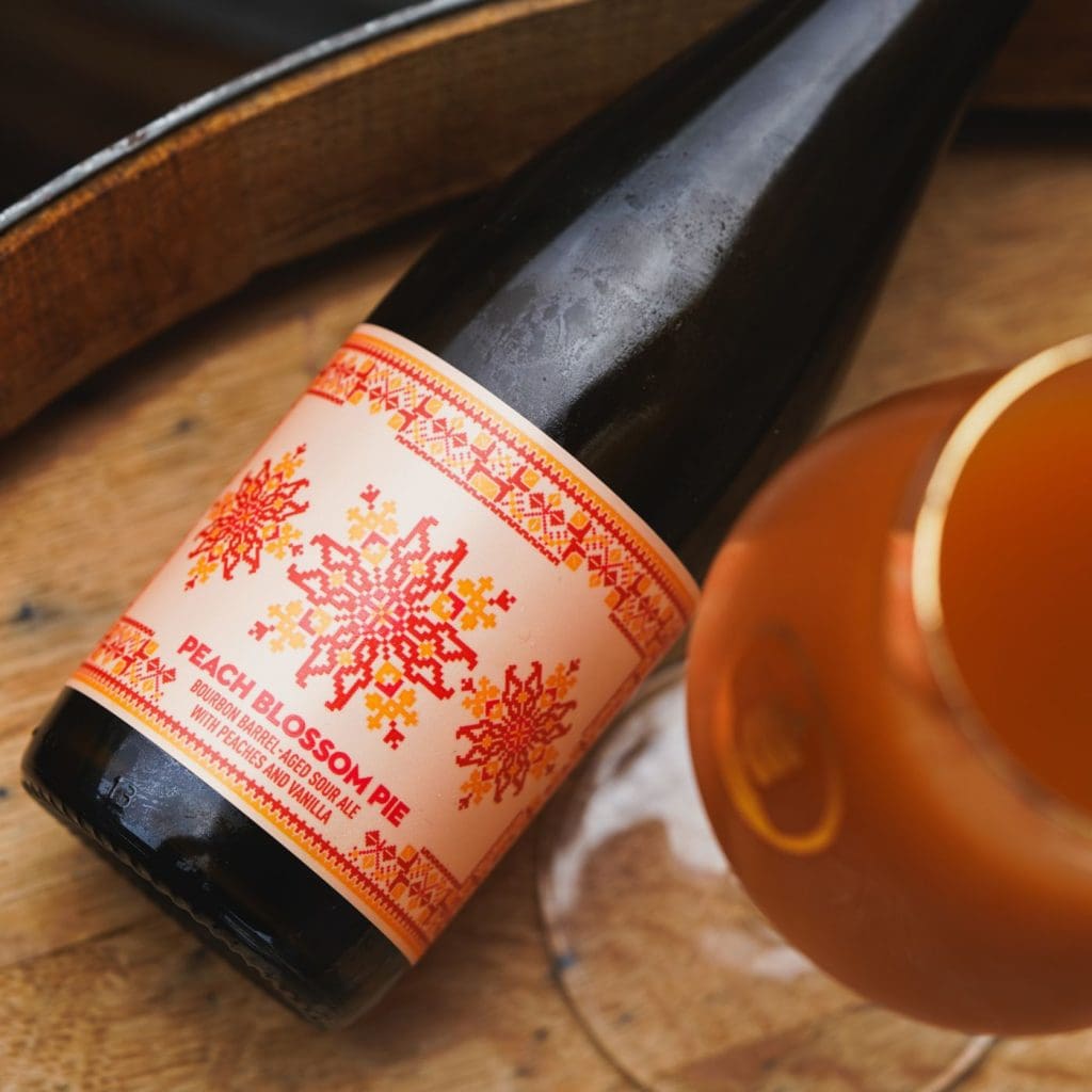 Top-down view of a bottle of Pure Project Peach Blossom Pie bourbon barrel-aged sour ale next to glass of beer