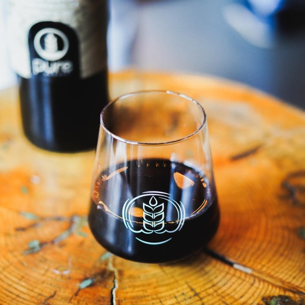 Image of glass of Pure Project Cabernet Sauvignon wine in the foreground with the bottle in the background