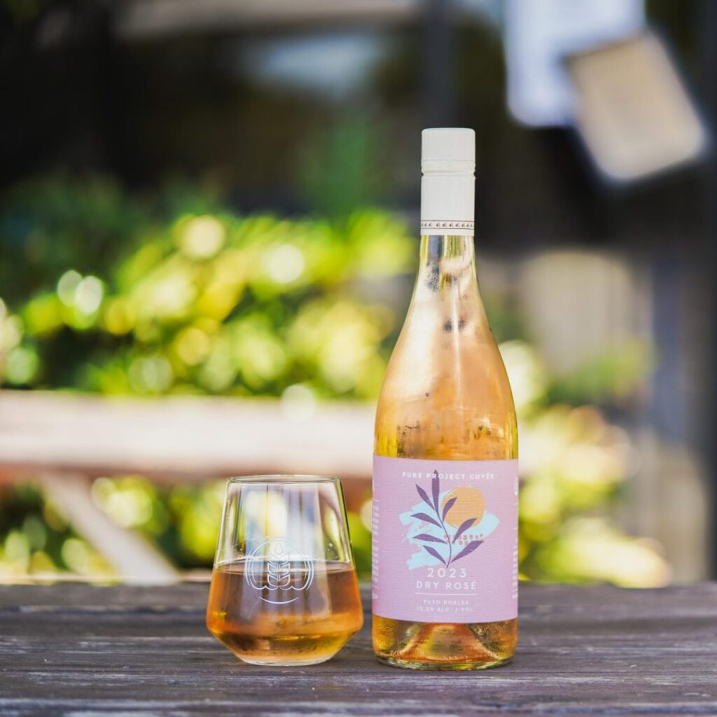 Bottle of Pure Project 2023 Dry Rosé next to a glass with the Pure Project logo filled with wine