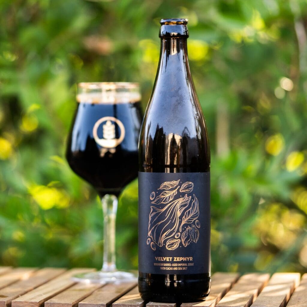 Image of bottle of Velvet Zephyr Bourbon Barrel-Aged Stout Next to a pour